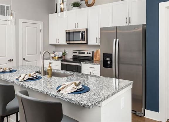 a kitchen with a marble counter top and a stainless steel refrigerator at The Flats at Southlawn Apartments, Lawrenceville, GA