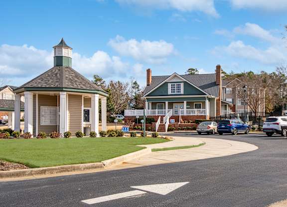 A small building with a green roof is in the middle of a road.