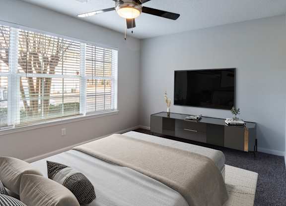 A bedroom with a bed, a television, and a window with blinds.