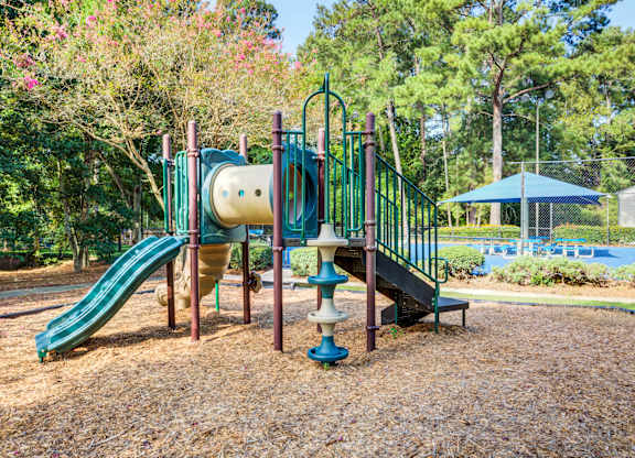 A playground with a green slide and a blue umbrella in the background.