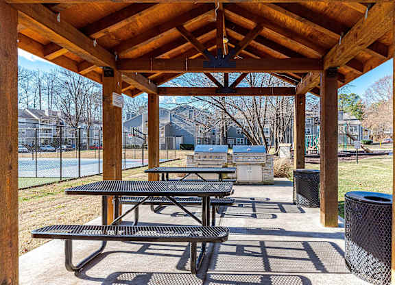 A wooden pavilion with picnic tables and a basketball court in the background.