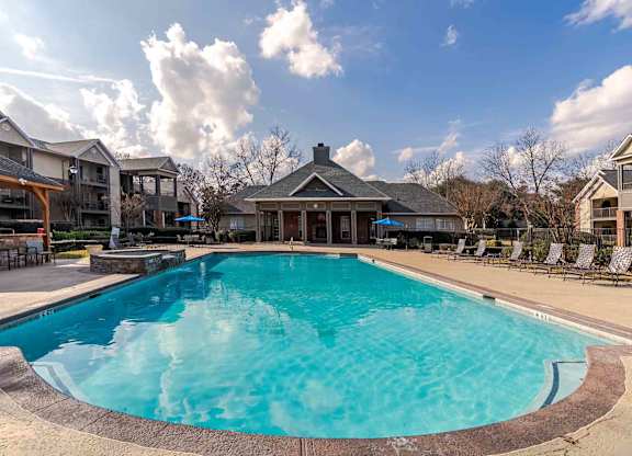 A large swimming pool in the middle of a resort surrounded by chairs.