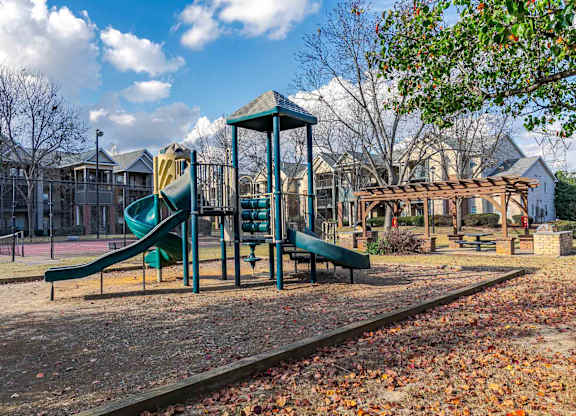 A playground with a green slide and a wooden structure.