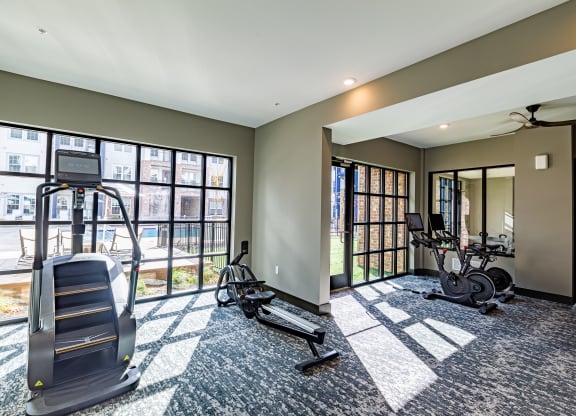 a gym with treadmills and weights in a room with windows at The Louis Apartment Flats, Louisville, Kentucky