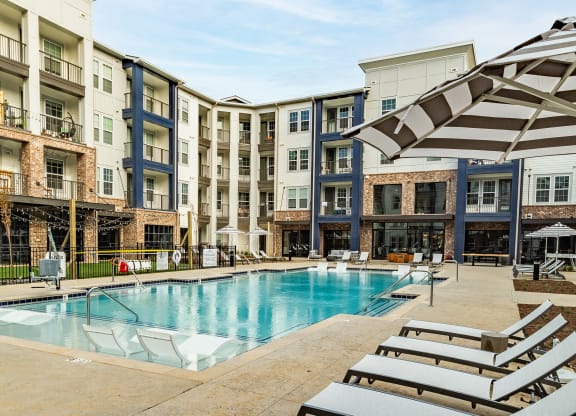 a swimming pool with beach chairs in front of an apartment building at The Louis Apartment Flats, Kentucky, 40241