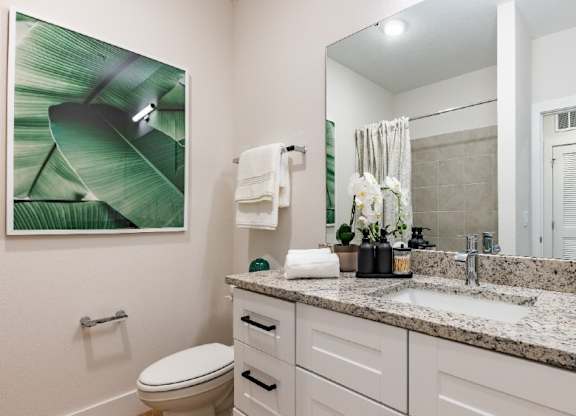 A bathroom with a toilet, sink, and a large leafy picture on the wall.