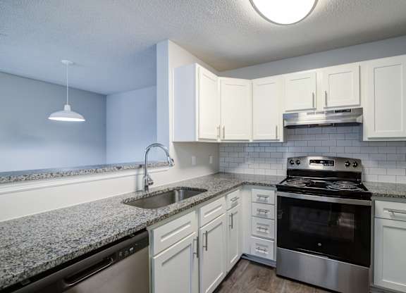 A kitchen with a stove, sink, and cabinets.