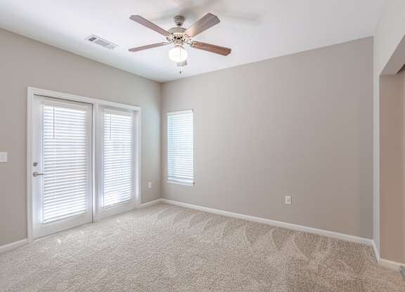 A room with a ceiling fan and two windows with blinds.