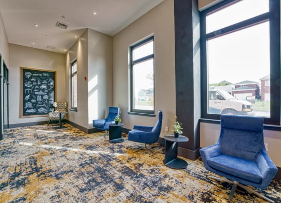 a lobby with blue chairs and a chalkboard on the wall and three large windows