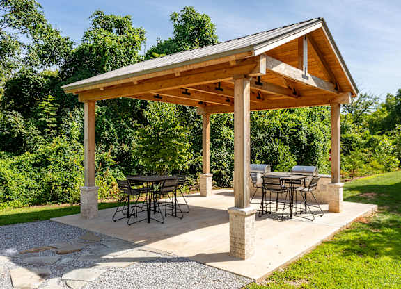A wooden pergola with a table and chairs is set up in a garden.