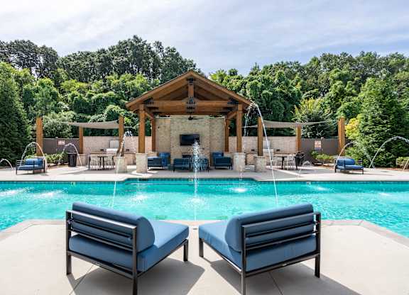 A pool with a wooden pavilion and lounge chairs.