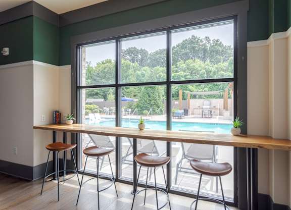 A room with a long table and chairs with a view of a pool and trees outside.