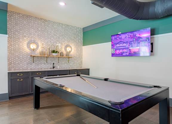 A pool table is in the middle of a room with a TV on the wall.