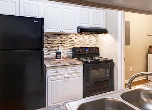 A black refrigerator is in a kitchen with white cabinets at Austin Chase Apartments, Macon