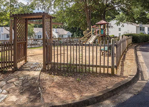 A playground with a wooden gate and a slide is surrounded by a fence.