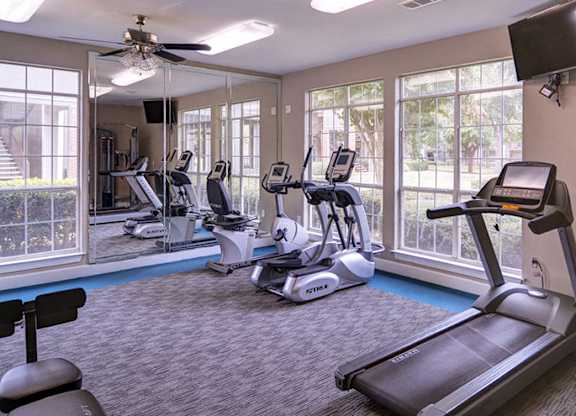 A spacious gym with treadmills, elliptical machines, and a television at Huntington Chase Apartments, Warner Robins, Georgia