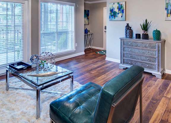 A living room with a black leather chair and a glass coffee table at Huntington Chase Apartments, Warner Robins, GA 31088