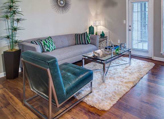 A living room with a grey couch, a green chair, and a glass coffee table at Huntington Chase Apartments, Warner Robins, GA