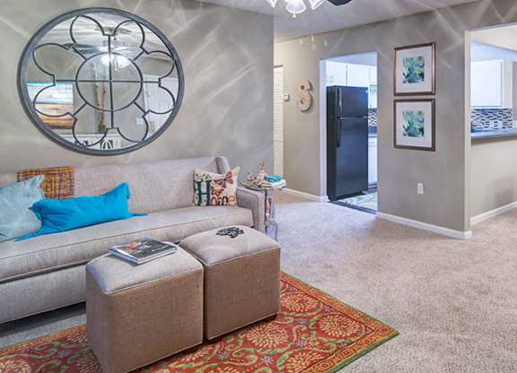 A living room with a grey couch, a round mirror, and a rug.