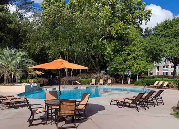 A pool surrounded by trees and chairs.