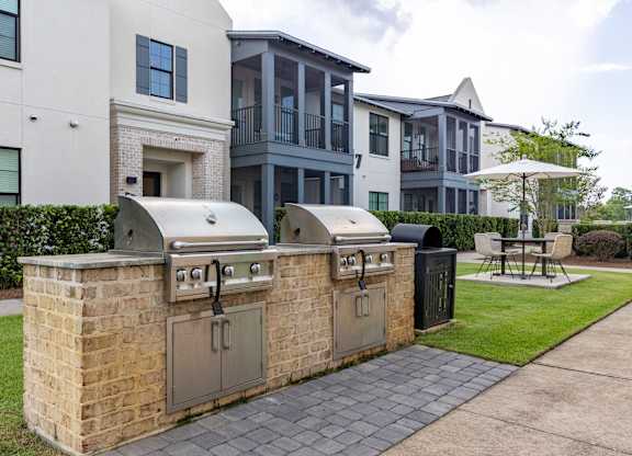 A brick BBQ grill is in front of a white and grey apartment building.