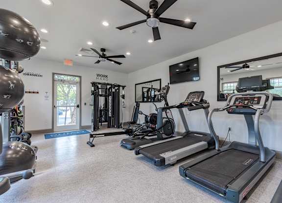 A spacious gym with treadmills, elliptical machines, and a ceiling fan.