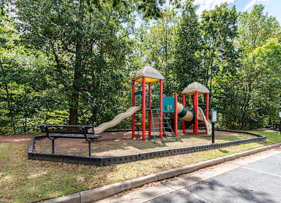 A playground with a red and green slide and a brown bench.
