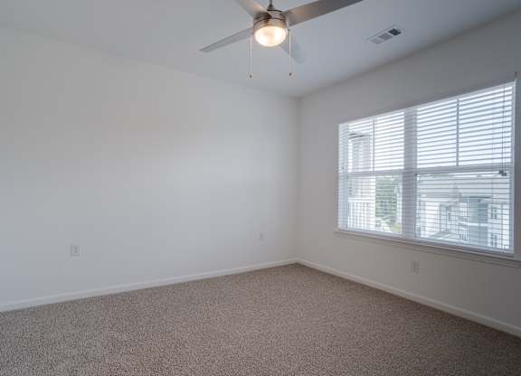 A room with a ceiling fan and a window with blinds.