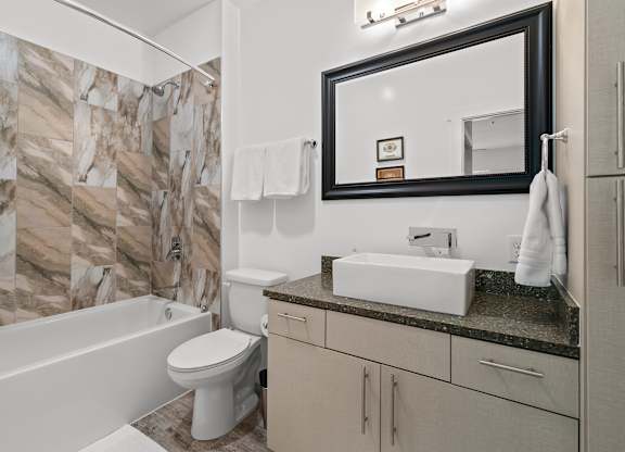 A bathroom with a marble patterned shower wall and a white bathtub.