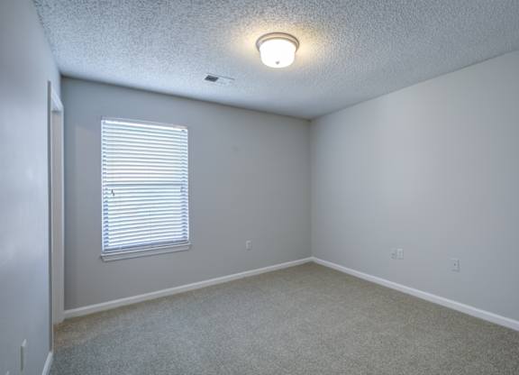 A room with a window covered by white blinds at Southland Station Apartments in Georgia, 31088