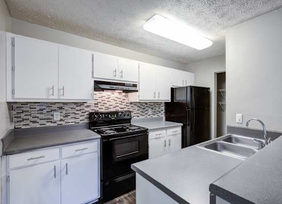 A kitchen with black and white cabinets and a tiled backsplash at Southland Station Apartments in GA, 31088