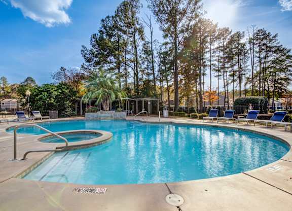 A large outdoor swimming pool surrounded by trees and lounge chairs at Southland Station Apartments in Warner Robins, 31088