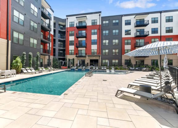 a swimming pool with chaise lounge chairs and umbrellas in front of an apartment building at Tapestry West, Richmond, VA