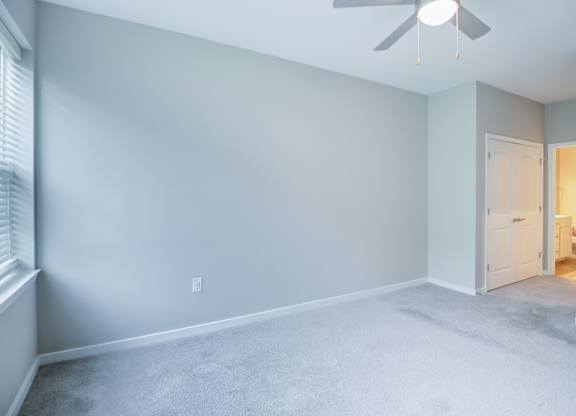 A room with a ceiling fan and a door leading to another room.