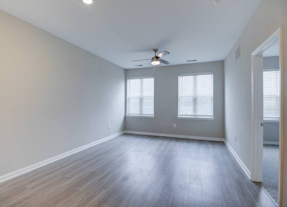 A room with a ceiling fan and two windows.