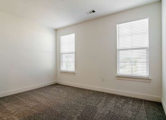 A room with carpeted floor and two windows.