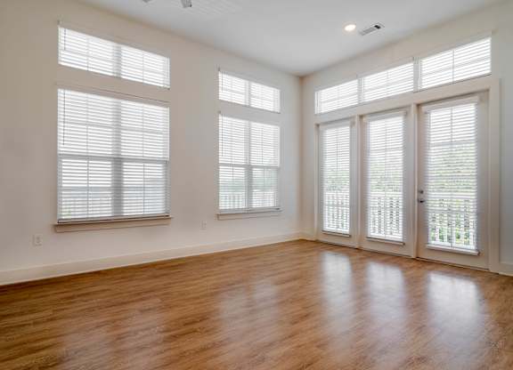 A room with wooden floors and three windows with blinds.