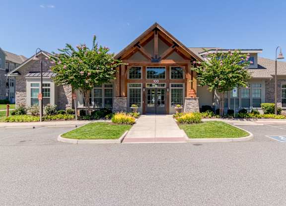 A building with a brown roof and a glass door is surrounded by a grassy area and a paved walkway.