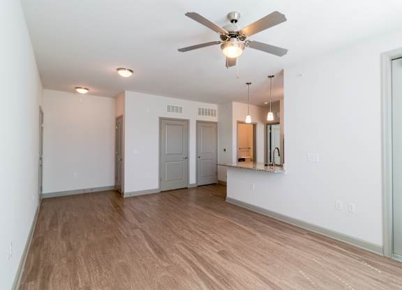 A room with a ceiling fan and light fixture, wooden flooring, and white walls.
