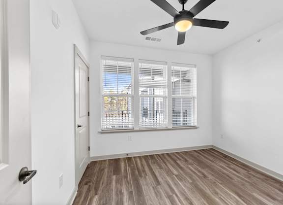 A room with a ceiling fan and a door leading to a balcony with a view of the outside.