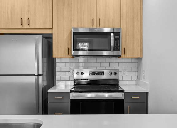 A kitchen with a stainless steel refrigerator, a microwave above the stove, and wooden cabinets.
