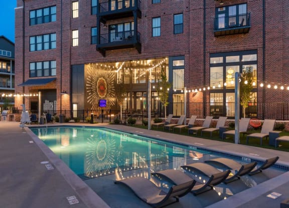 a swimming pool with chaise lounge chairs and a brick building in the background at Livingston Flats Apartments, Chesterfield
