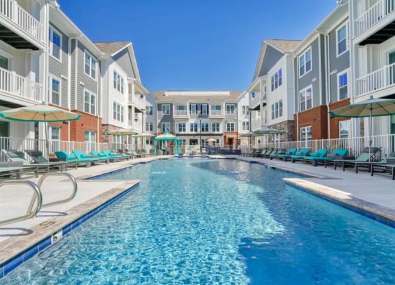 a swimming pool with chaise lounge chairs and umbrellas in front of an apartment building at Artistry at Winterfield Apartments, Midlothian, VA
