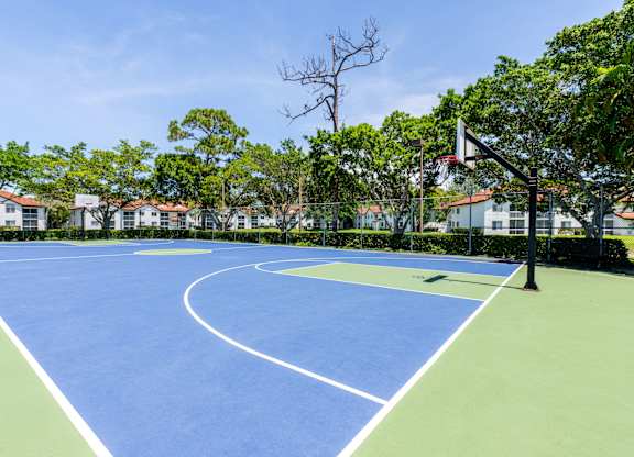 A blue tennis court surrounded by green grass and trees.