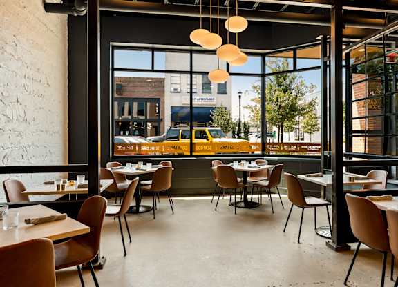 A restaurant with tables and chairs and a view of the street outside.