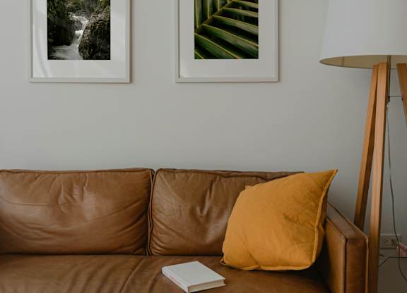 A brown couch with a yellow pillow and a book on it.