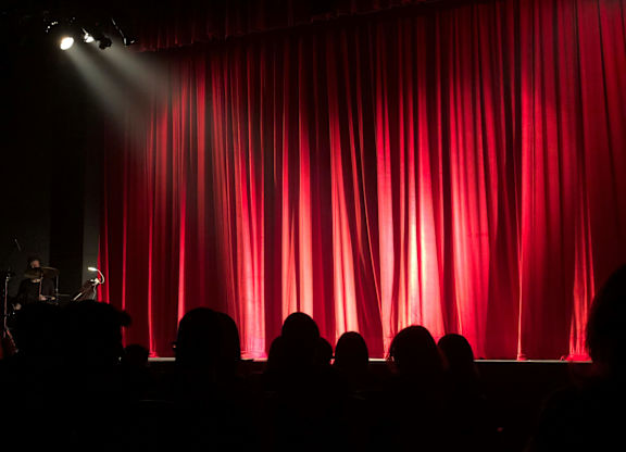 A red curtain on a stage with people watching.