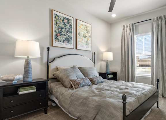 A bedroom with a large bed, a nightstand with a lamp, and two wall art pieces.
