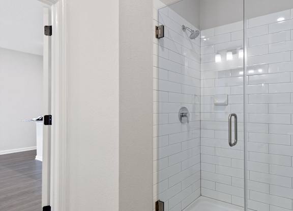 A white tiled shower with a glass door and a silver handle.