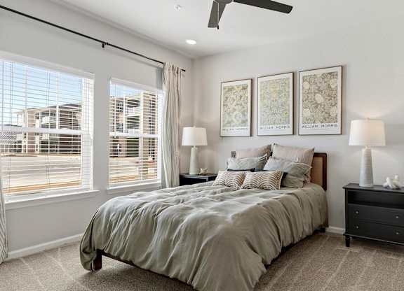 A bedroom with a large bed, a ceiling fan, and a view of a street outside the window.